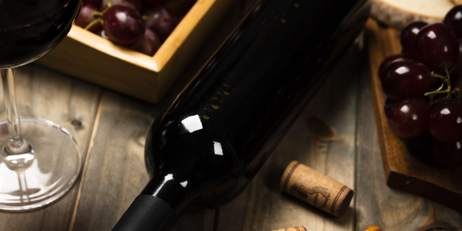 Botella de vino tinto, copa y tabla de tapas sobre una mesa de madera