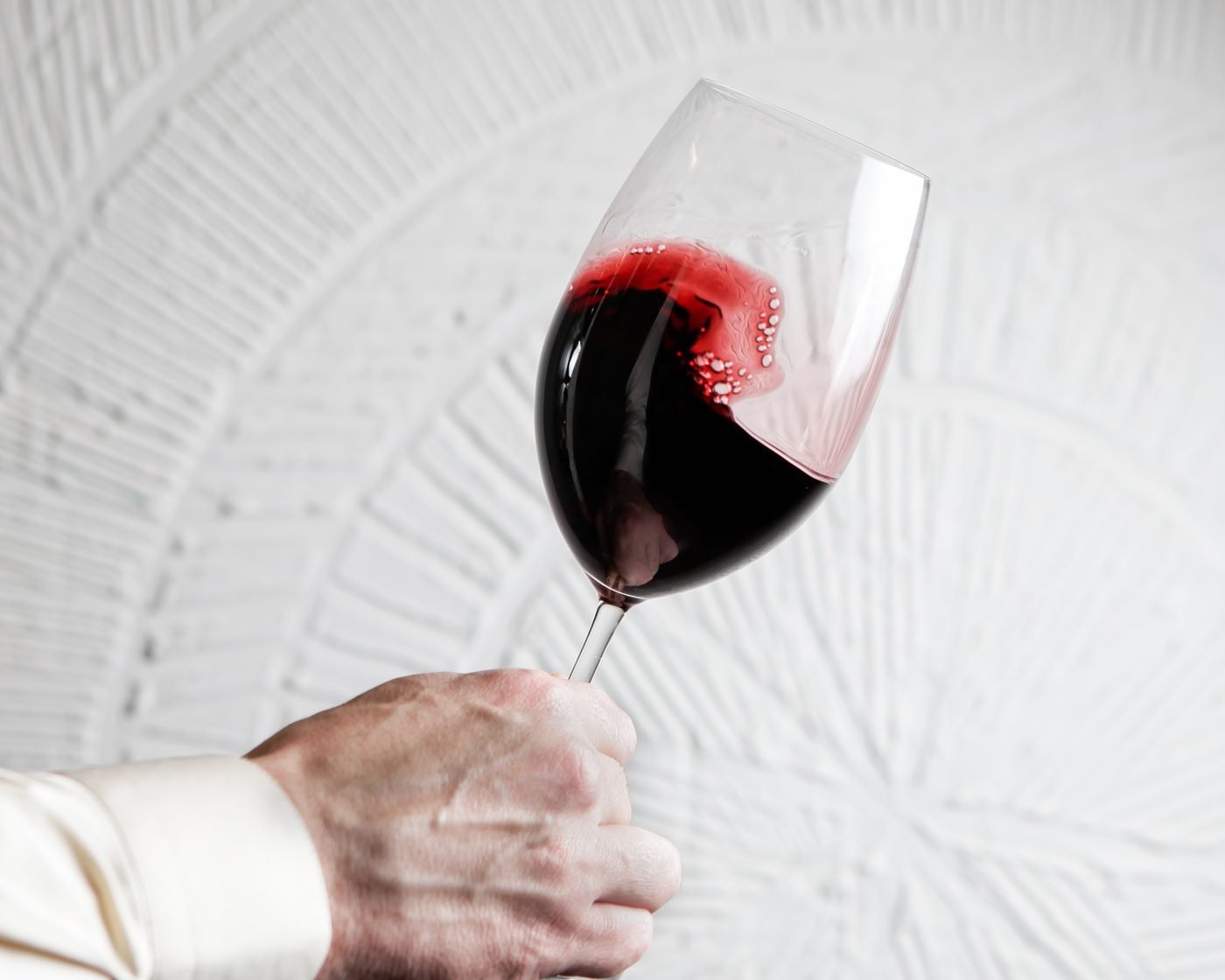 Mano sujetando una copa de vino tinto inclinada sobre un fondo claro